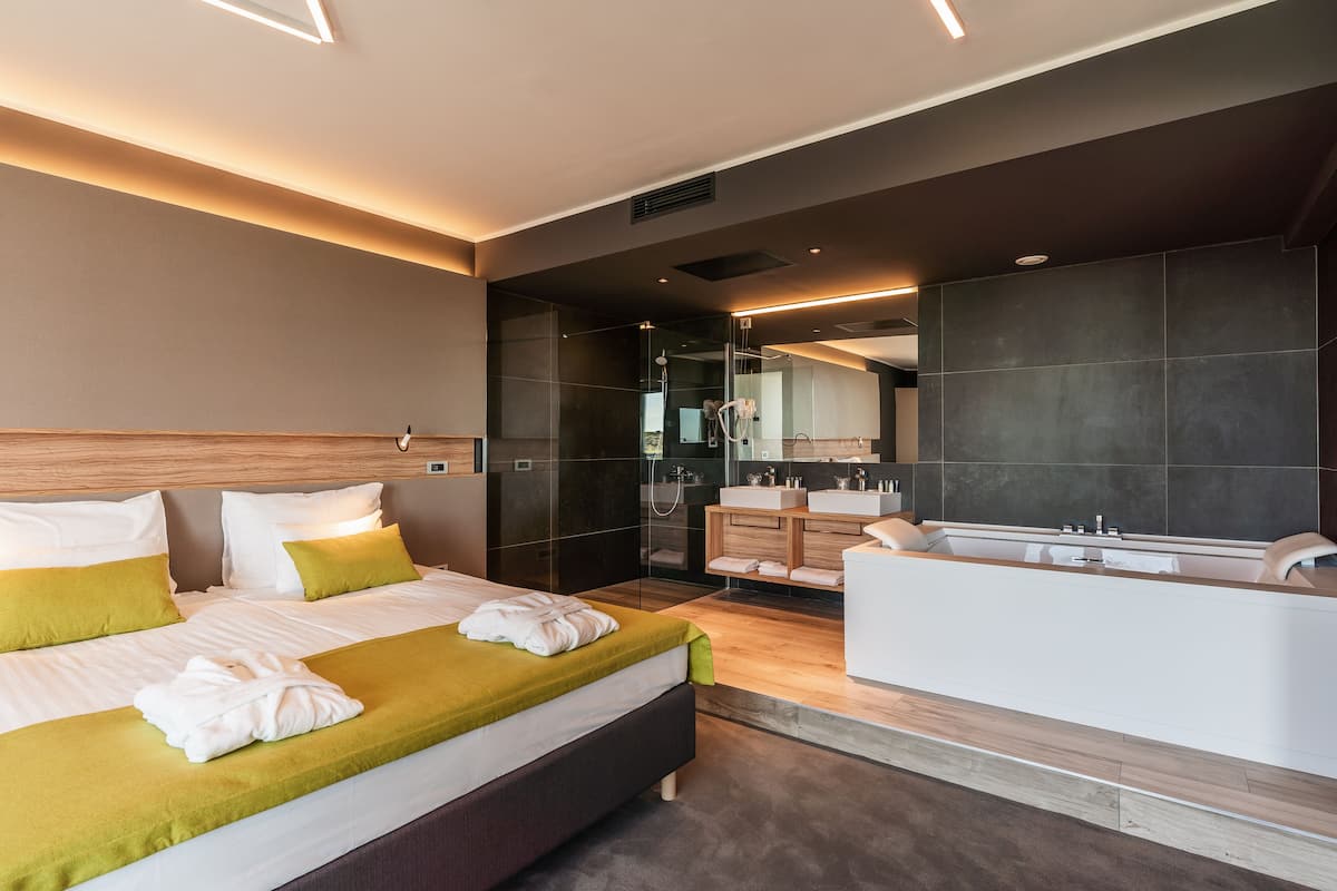 A modern hotel room with a large bed, a separate bathroom with a bathtub, and a large mirror.