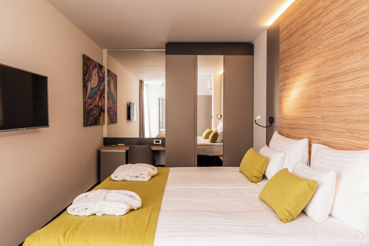 A hotel room with a bed, a desk, a chair, a TV, and a mirror.