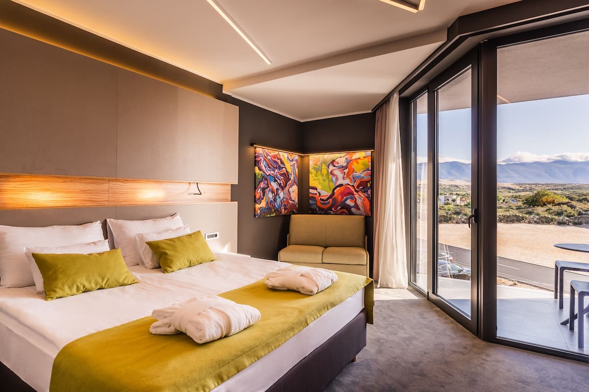A modern hotel room with a large bed, a sofa, and a balcony with a view of mountains.