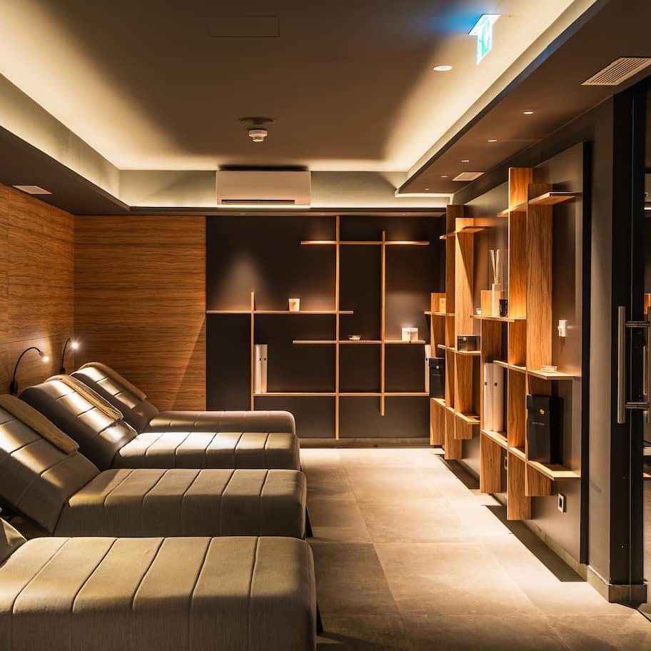 A modern spa area with massage chairs, wooden shelves, and a glass partition.