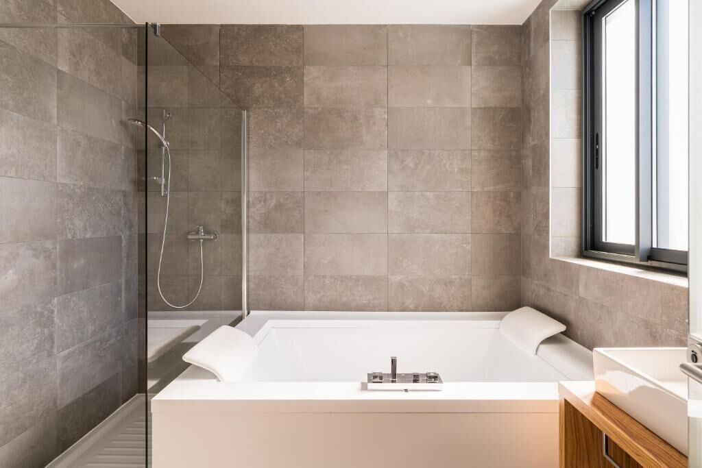 A modern bathroom with a glass-enclosed shower, a large white bathtub, and a wooden vanity.