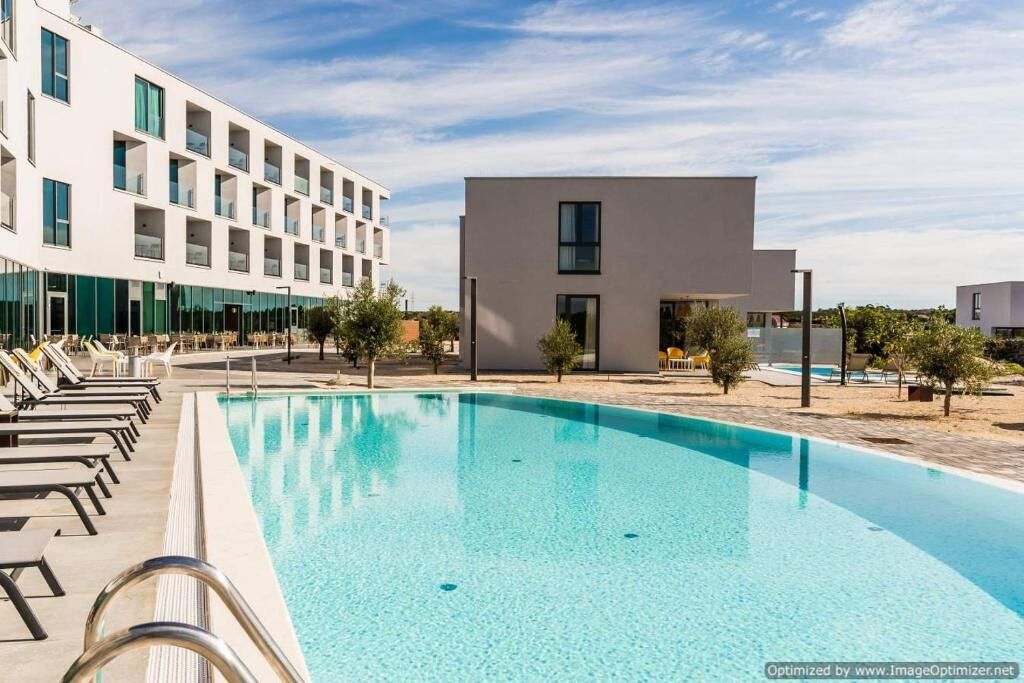 Un hotel moderno con piscina, sillones de descanso y un pequeño edificio de techo plano.