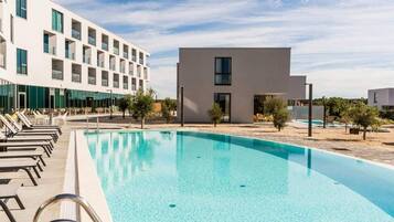 A modern hotel with a swimming pool, lounge chairs, and a small building with a flat roof.