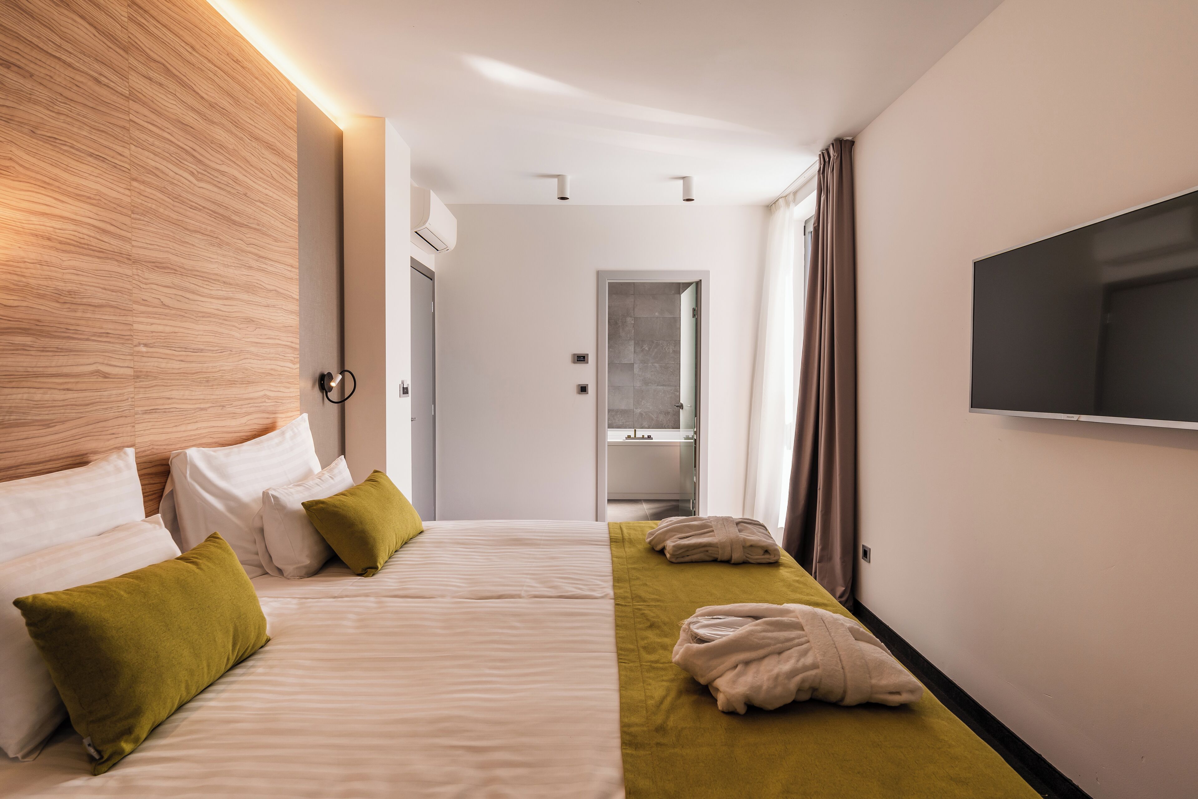 A hotel room with a bed, pillows, a TV, and a bathroom visible through an open door.