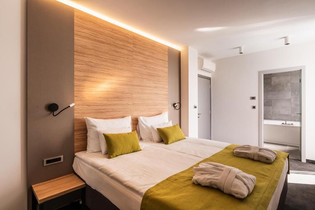 A modern hotel room with a large bed, a wooden headboard, and a bathroom visible through an open door.