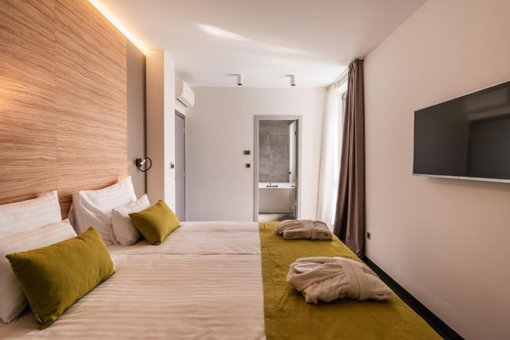Et hotelværelse med en stor seng, et tv ophængt på væggen og et badeværelse, der kan ses igennem en åben dør.