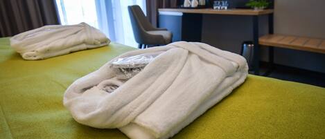 Habitación de hotel con una colcha verde, una toalla blanca doblada y un pequeño objeto envuelto en plástico sobre la cama.