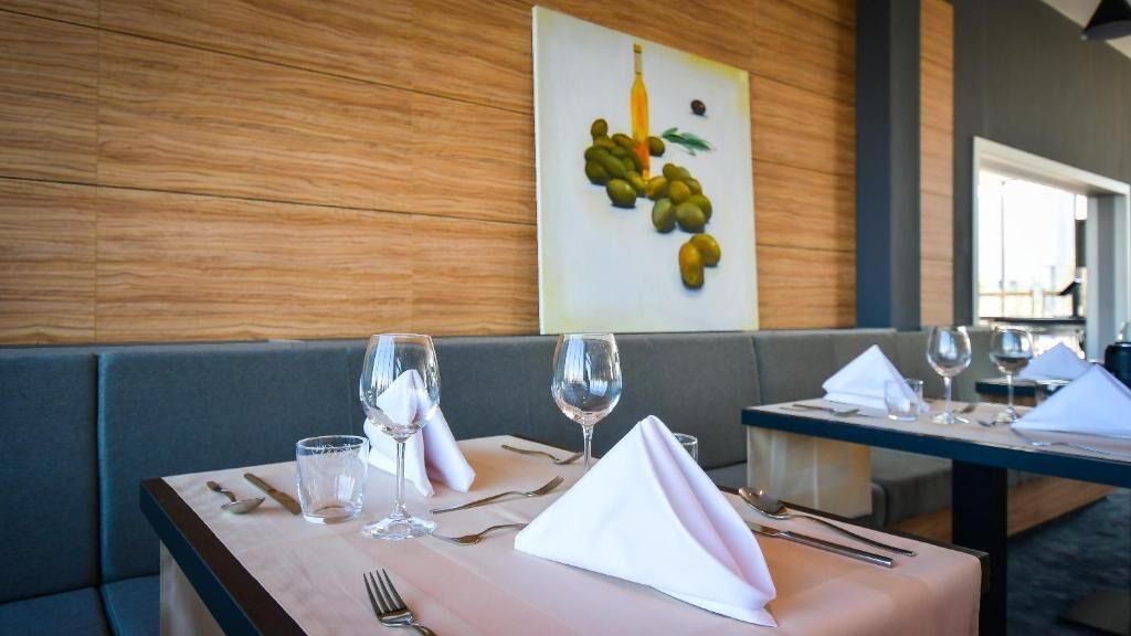 A dining table set with wine glasses, cutlery, and a napkin, with a wooden wall and a painting in the background.