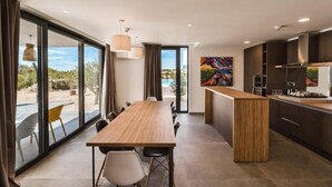 A modern kitchen with a wooden table and chairs, large windows, and a view of the outdoors. - Hotel Olea (Novalja)