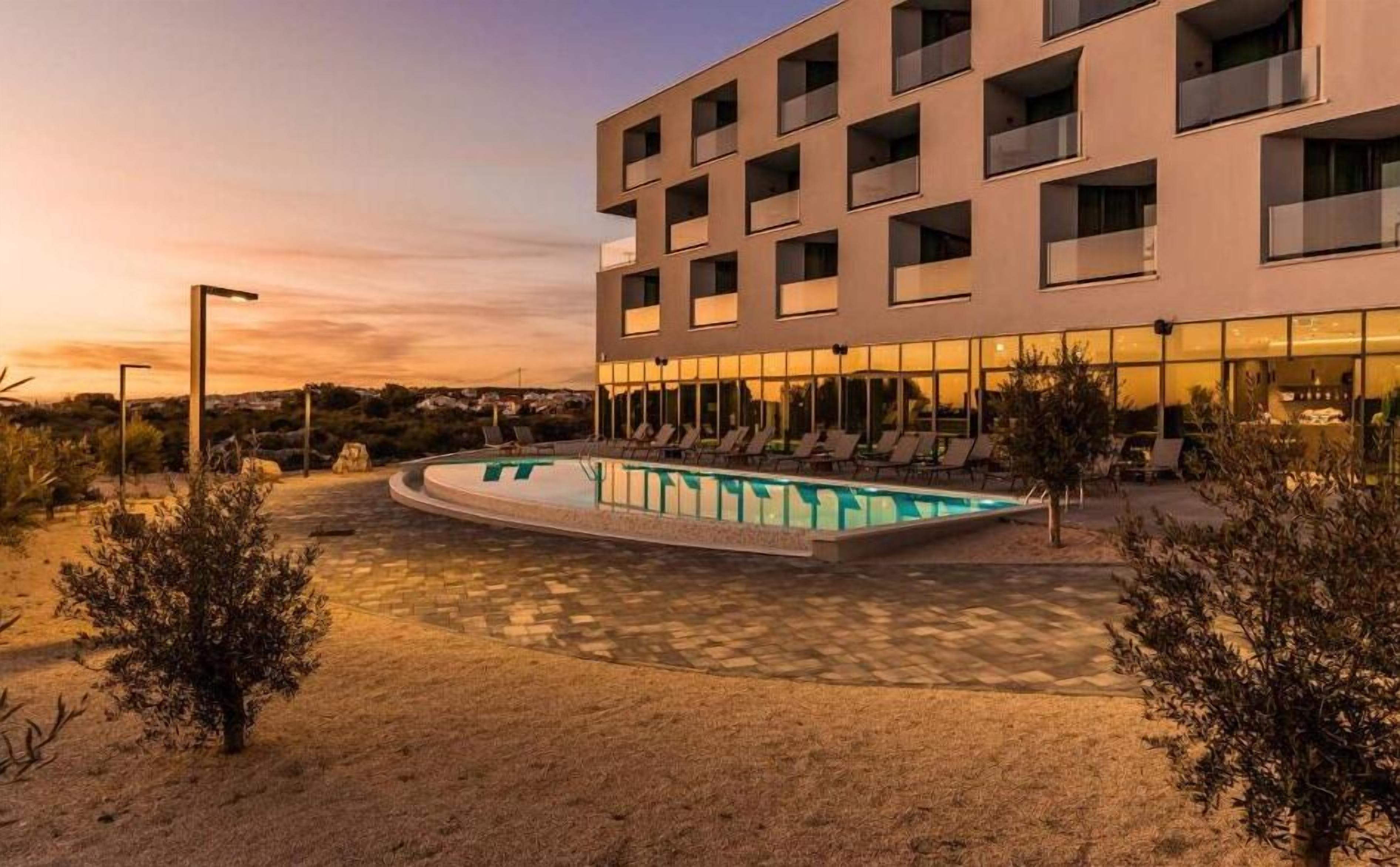 A modern hotel with a pool, sun loungers, and a desert landscape.