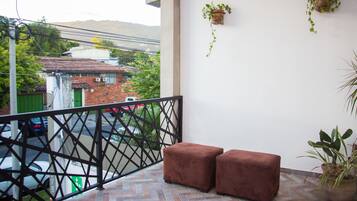 A balcony with two brown ottomans, a potted plant, and hanging plants on the wall.
