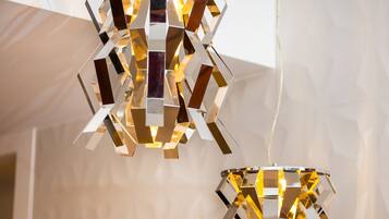 Two geometric pendant lights with a reflective surface, hanging from a ceiling with a textured wall in the background.