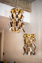 Two geometric pendant lights with a reflective surface, hanging from a ceiling with a textured wall in the background.
