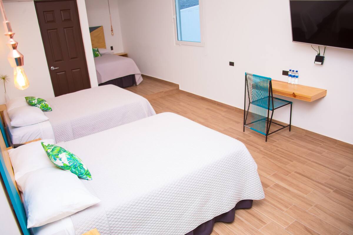 Een hotelkamer met twee bedden, een aan de muur bevestigde televisie, een houten bureau en een stoel.