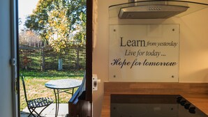 A kitchen with a glass door leading to a patio, a stainless steel range hood, and a motivational quote on the wall. - Mollett's Farm (Saxmundham)