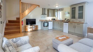 A modern kitchen with a microwave, oven, and dishwasher, a wooden staircase, and a living area with a sofa and a coffee table. - Mollett's Farm (Saxmundham)