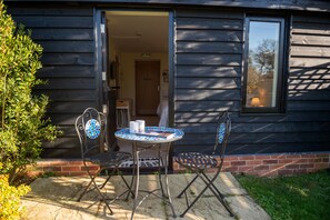 A patio with a table and two chairs, a door leading inside, and a window with a view. - Mollett's Farm (Saxmundham)