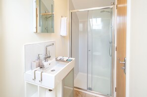 A modern bathroom with a glass-enclosed shower, a white sink with a mirror above it, and a wooden door. - Mollett's Farm (Saxmundham)