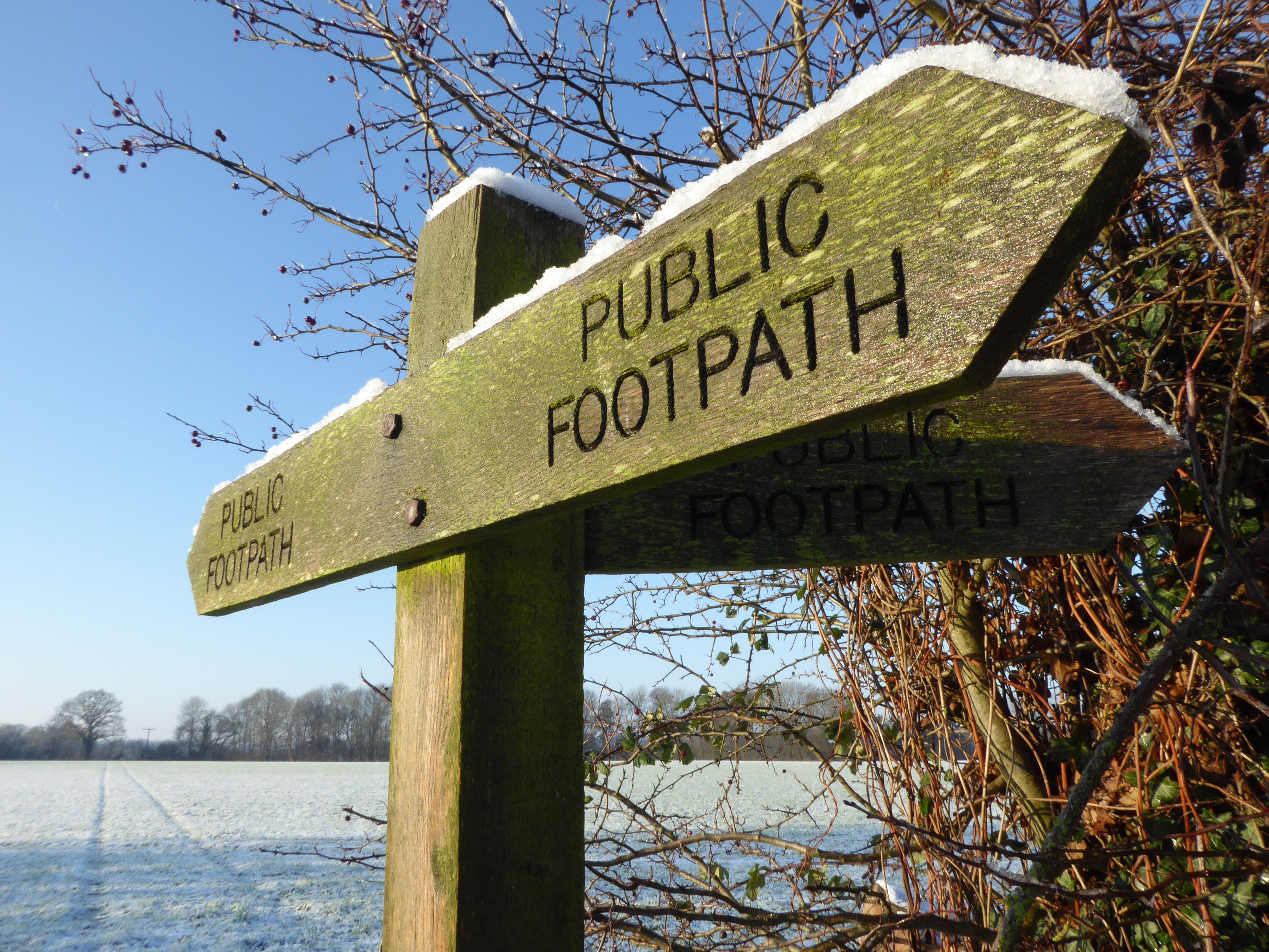 A wooden public footpath sign with directional arrows.