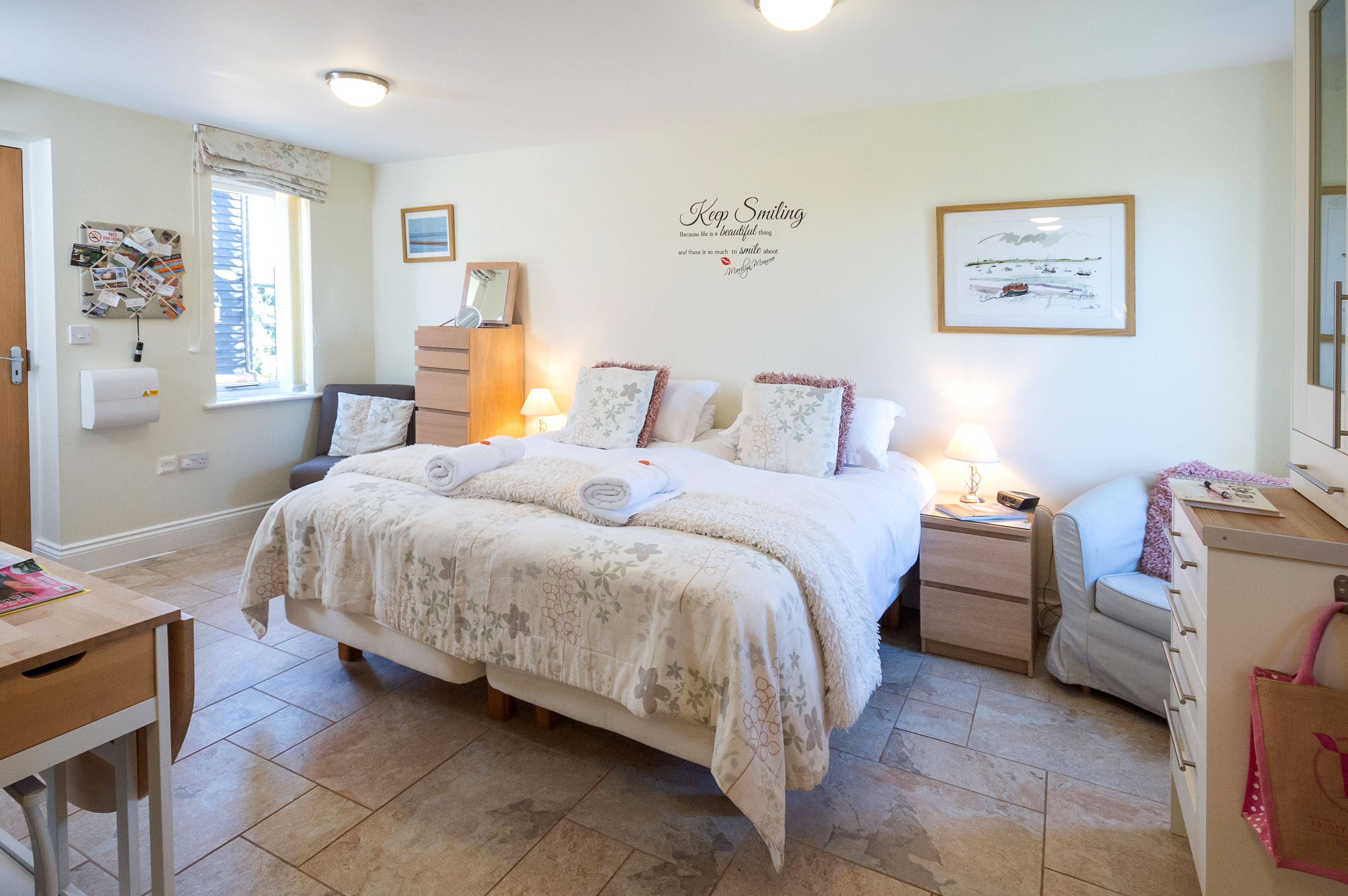 A neatly arranged bedroom with a bed, bedside tables, a desk, and a chair.