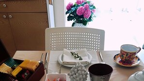 A neatly set dining table with a white tablecloth, a bowl of red items, a silver teapot, and a cup with a colorful design. - Villa Sece - Luxury Rooms (Agrigento)
