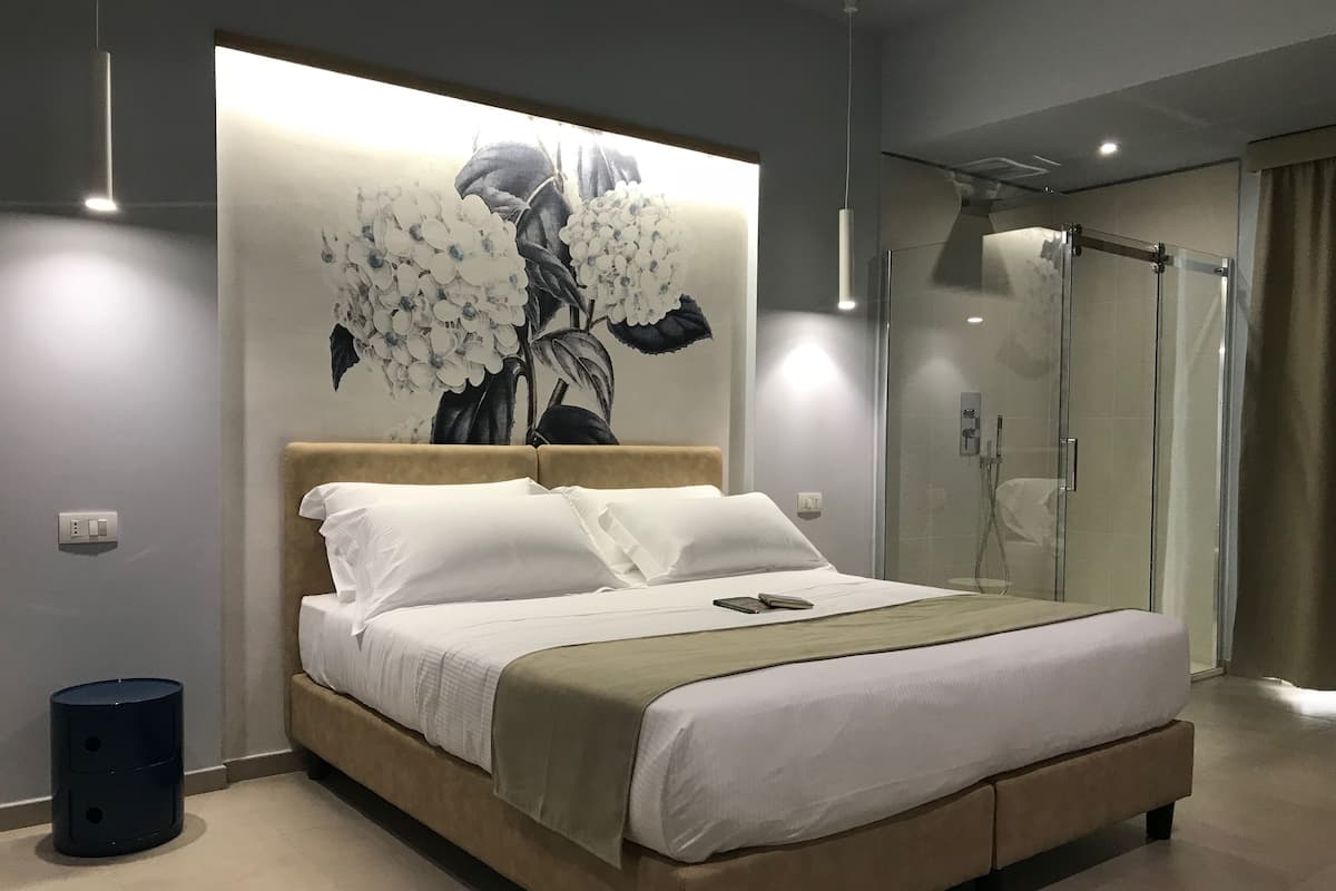 A modern bedroom with a large bed, a glass shower enclosure, and a wall-mounted artwork of flowers.
