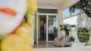 Un patio moderno con una puerta corrediza de vidrio que da a una cocina, rodeado de plantas en macetas y un espacio de estar con mesa y sillas.