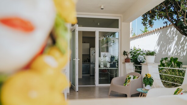 A modern patio with a sliding glass door leading to a kitchen, surrounded by potted plants and a seating area with a table and chairs. - Villa Sece - Luxury Rooms (Agrigento)