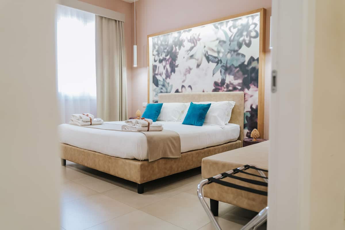 A double bed with white and blue pillows, a bedside table with a lamp, and a view of the room's interior.