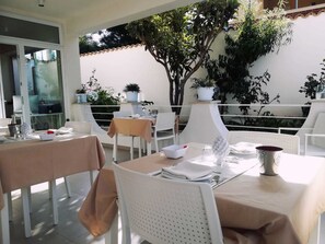 Un área de comedor al aire libre con sillas y mesas blancas, plantas en macetas y vistas al follaje circundante.