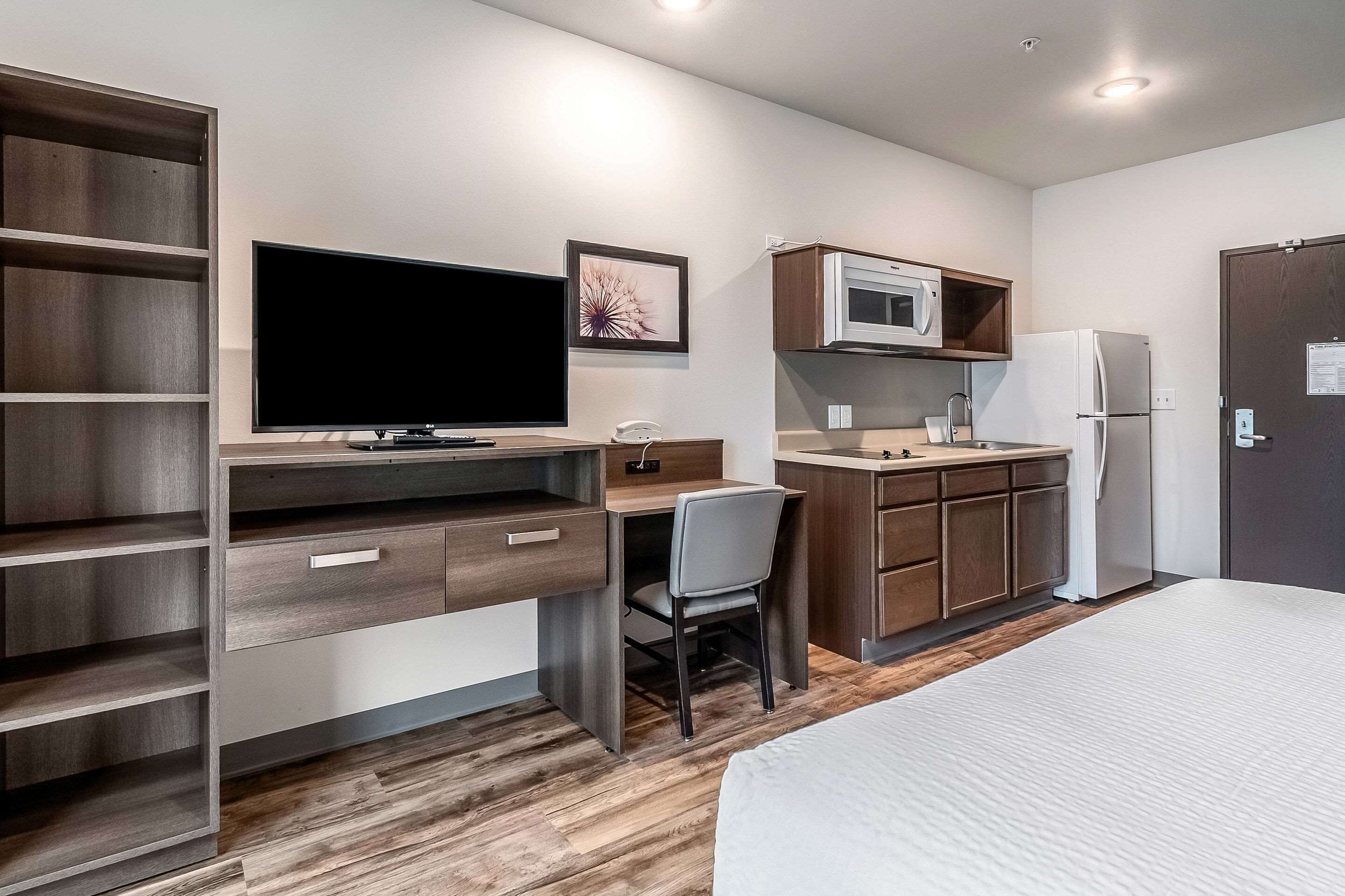 Una habitación de hotel moderna con un escritorio de madera, un televisor de pantalla plana, microondas, refrigerador y una cama.