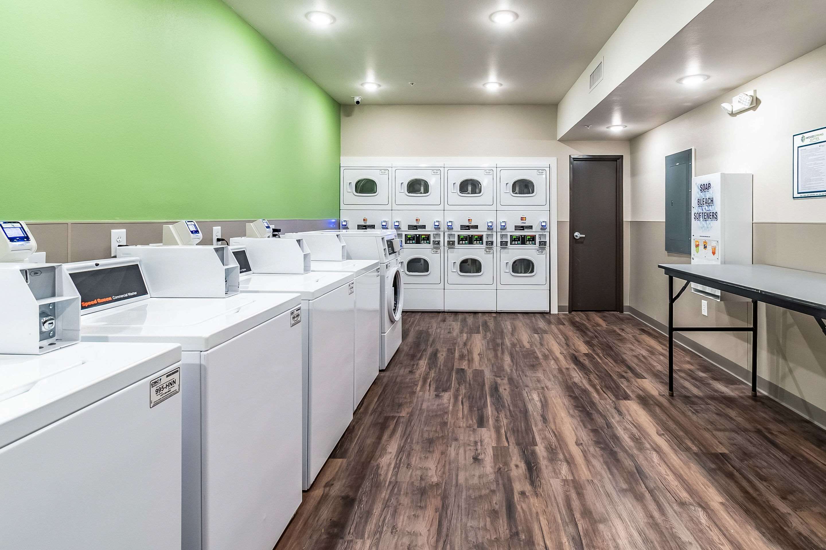 A laundry facility with multiple washing machines, a control panel, and a sign indicating the use of soap, bleach, and softeners.