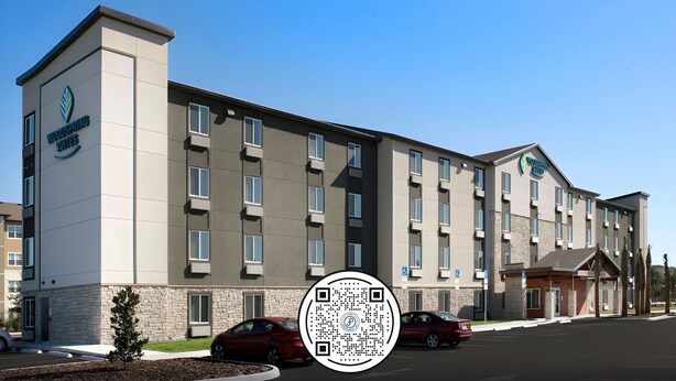 Un bâtiment d’hôtel moderne, doté d’un toit plat, de nombreuses fenêtres et d’un parking où sont garées des voitures.