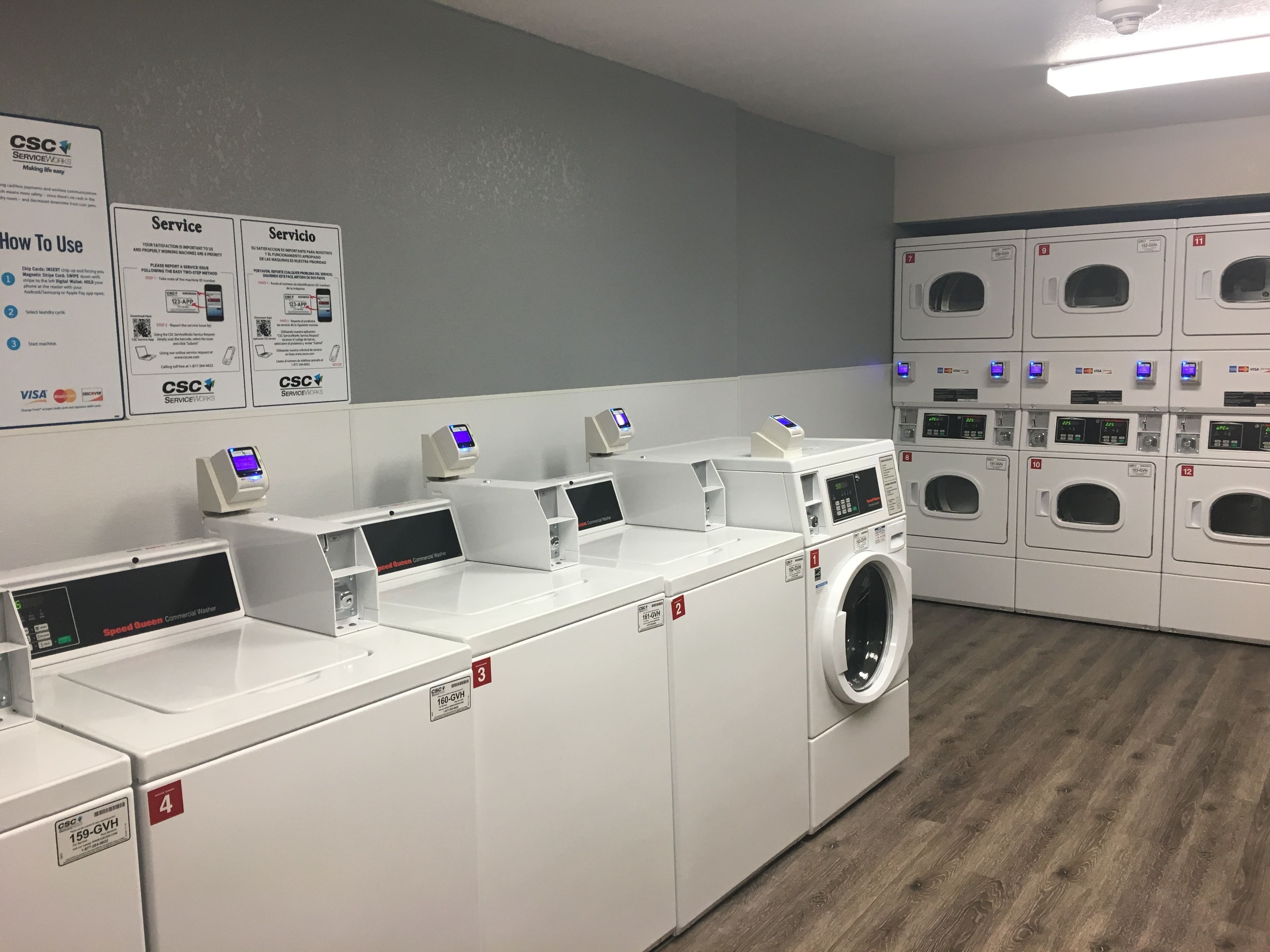 Une laverie équipée de plusieurs machines à laver et de plusieurs séchoirs, de bornes de paiement numériques et de panneaux d’information.
