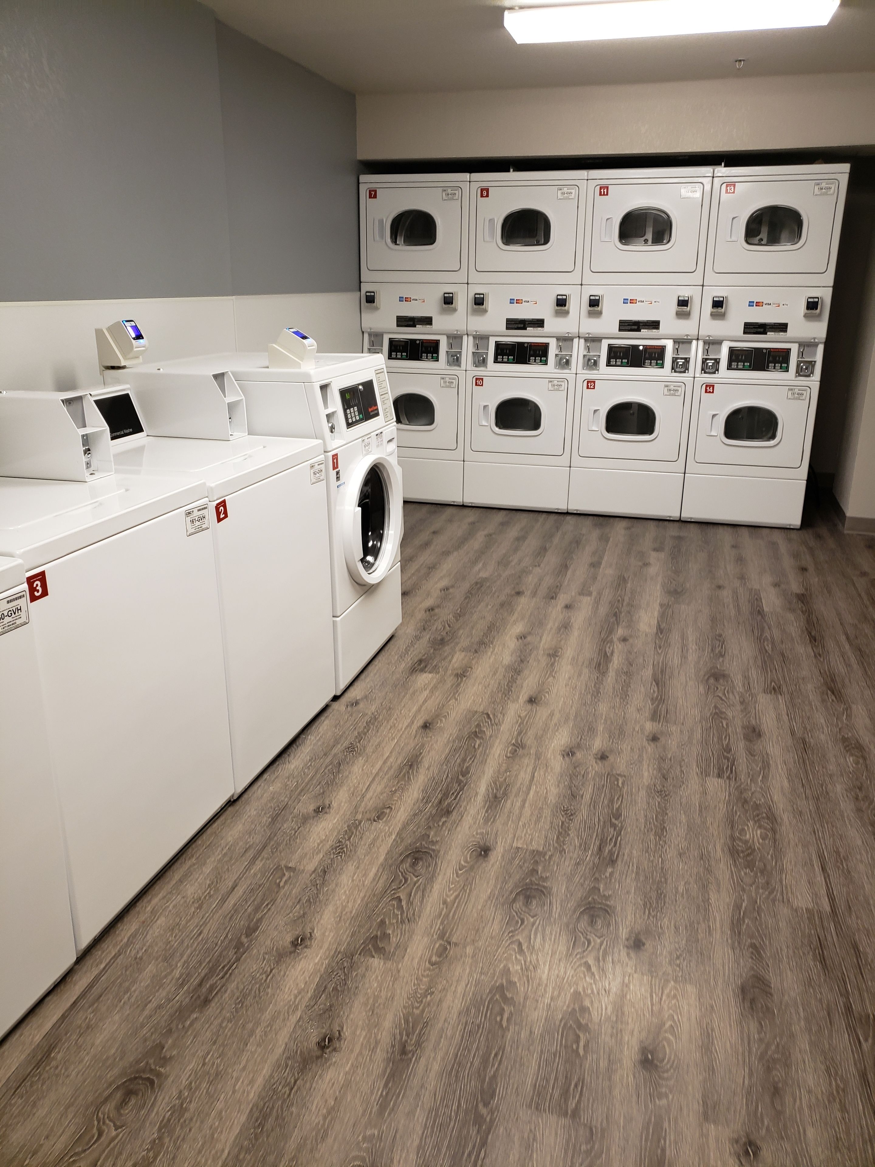 Un cuarto de lavandería con varias lavadoras y secadoras dispuestas en filas.