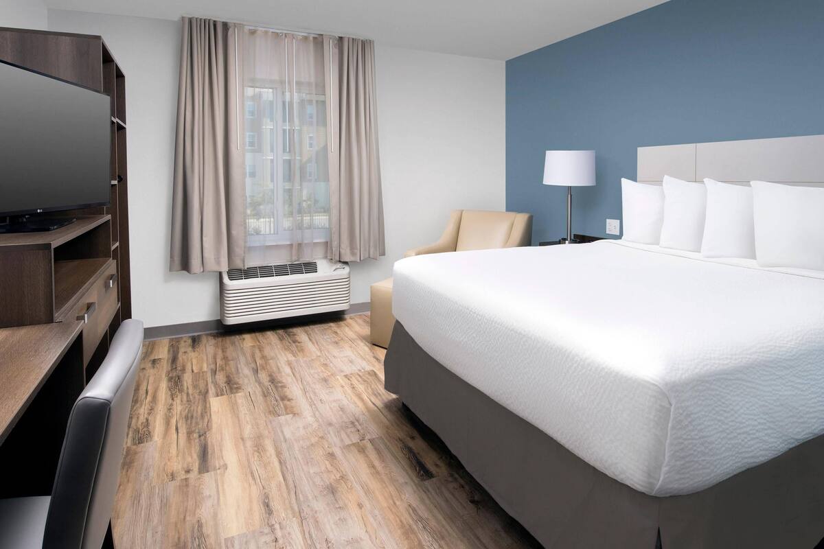 A hotel room with a large bed, a TV, a desk, and a window with curtains.