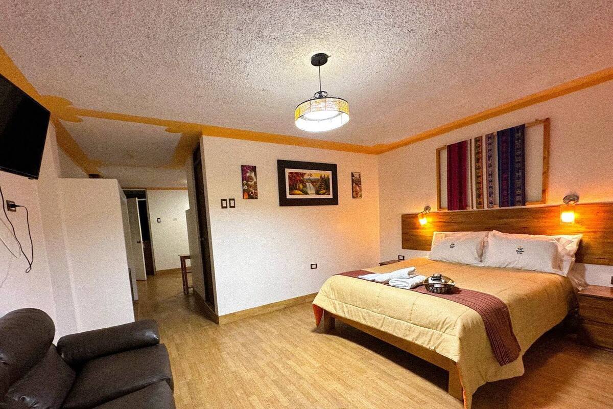 A hotel room with a bed, bedside tables, a chair, and artwork on the walls.