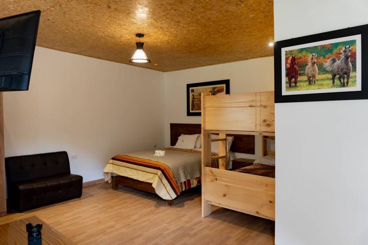 A bedroom with a bunk bed, a single bed, a wooden headboard, a wooden floor, a black leather sofa, and a ceiling light fixture.