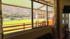 A room with a large window overlooking a green field and a building with orange walls. - Tambo Lodge Canta (Canta)