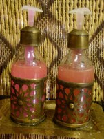 Dos botellas de vidrio con tapas metálicas y líquido rosado, sobre una superficie de madera con textura tejida.
