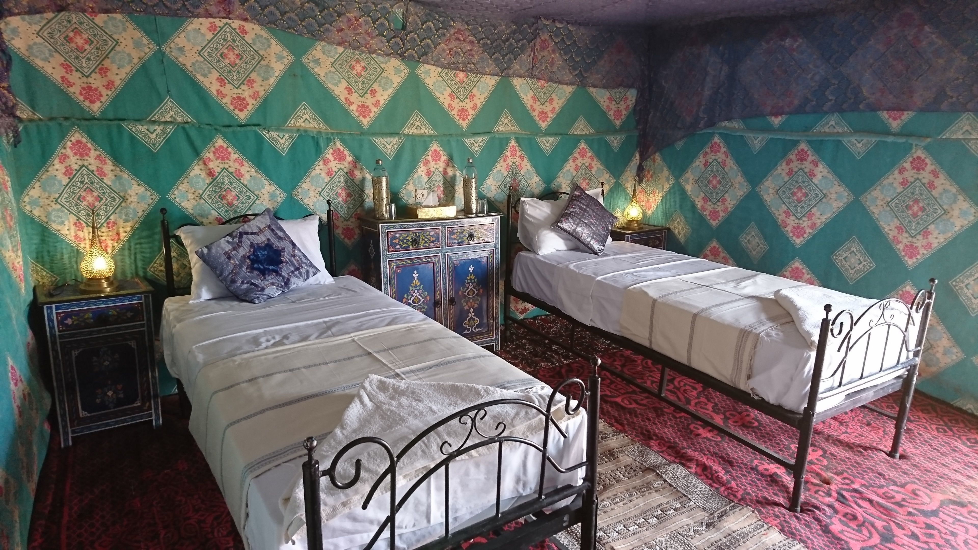Una camera tradizionale con due letti singoli, tende a fantasia e un mobile decorativo.