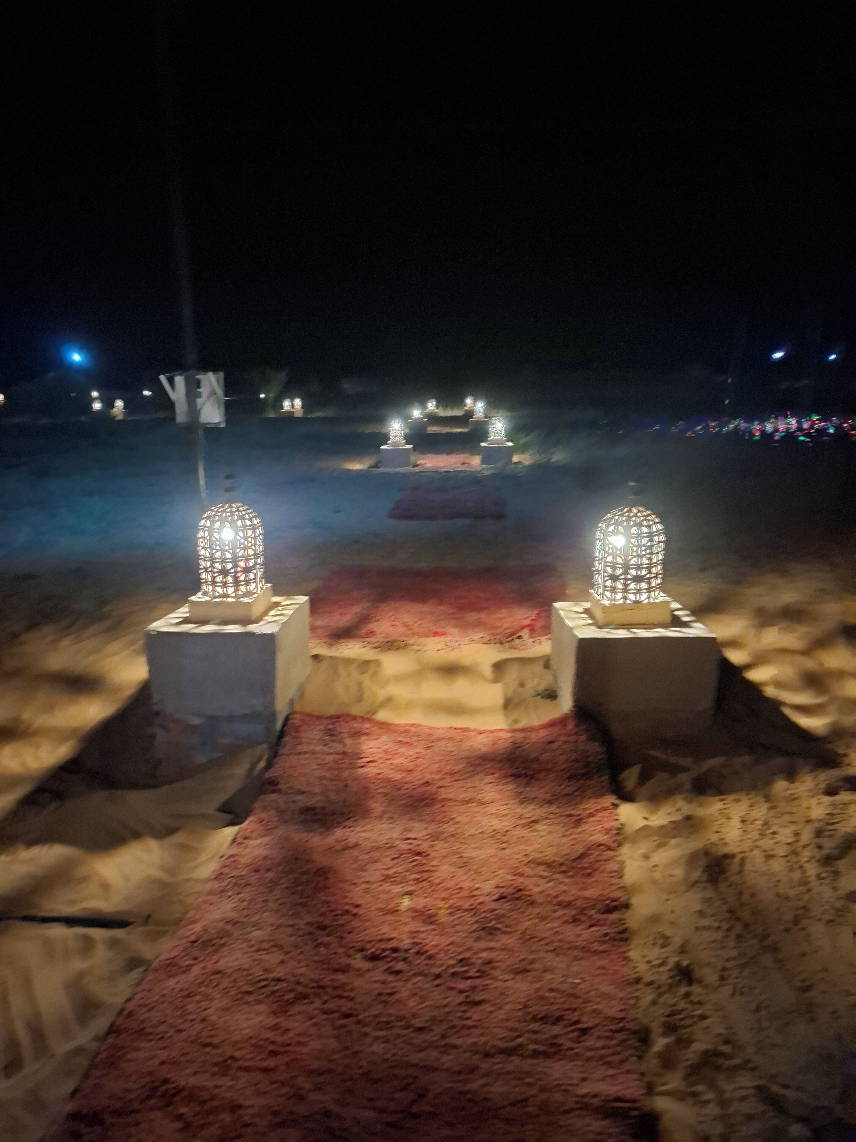 A pathway leading to a structure with two illuminated lanterns on either side.