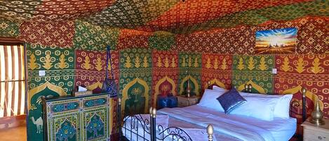 Una habitación con una cama, una mesita de noche, un mueble decorativo y una pared con estampado.