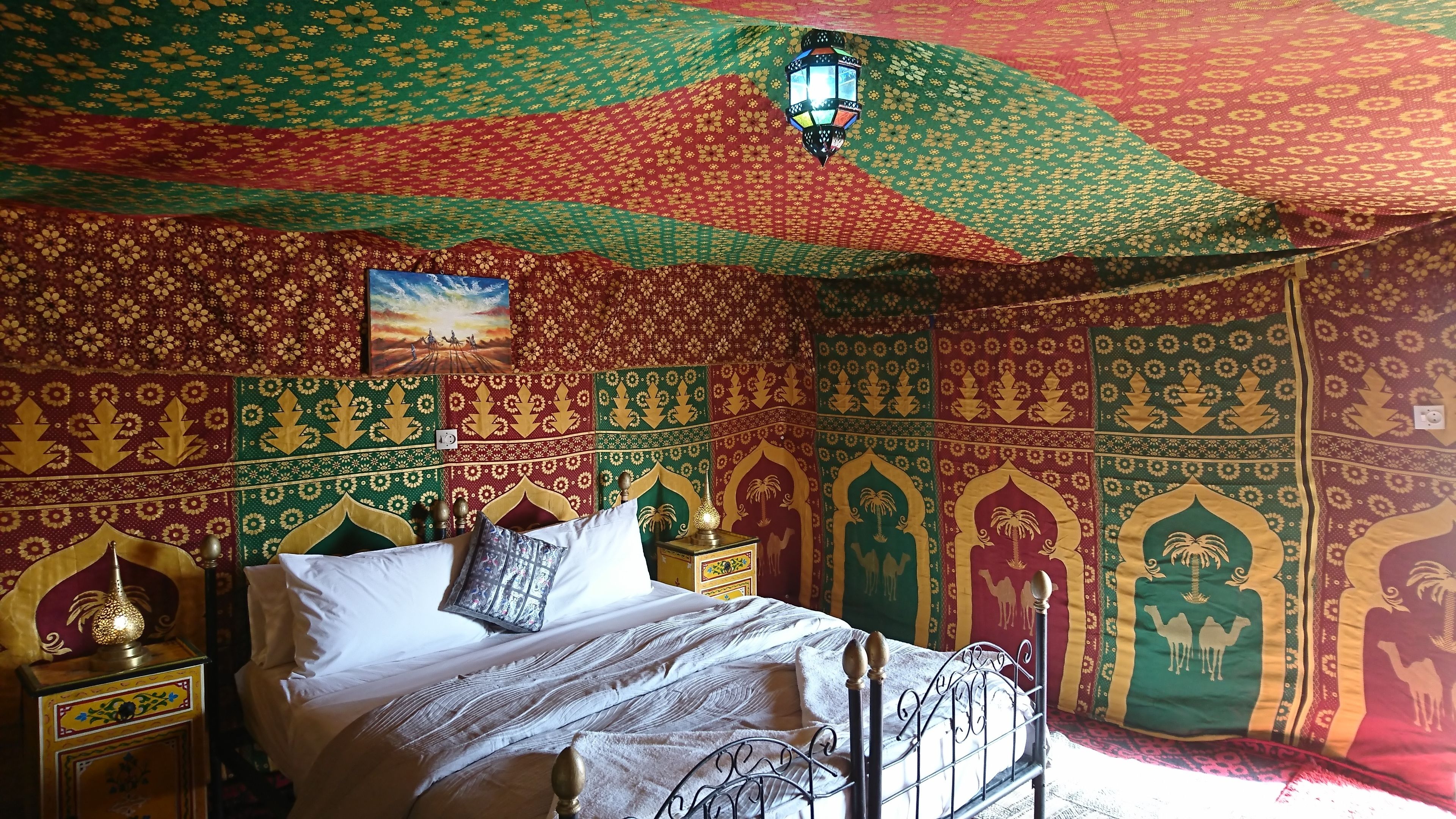 A room with a bed, a nightstand, a wall hanging, and a hanging lantern.
