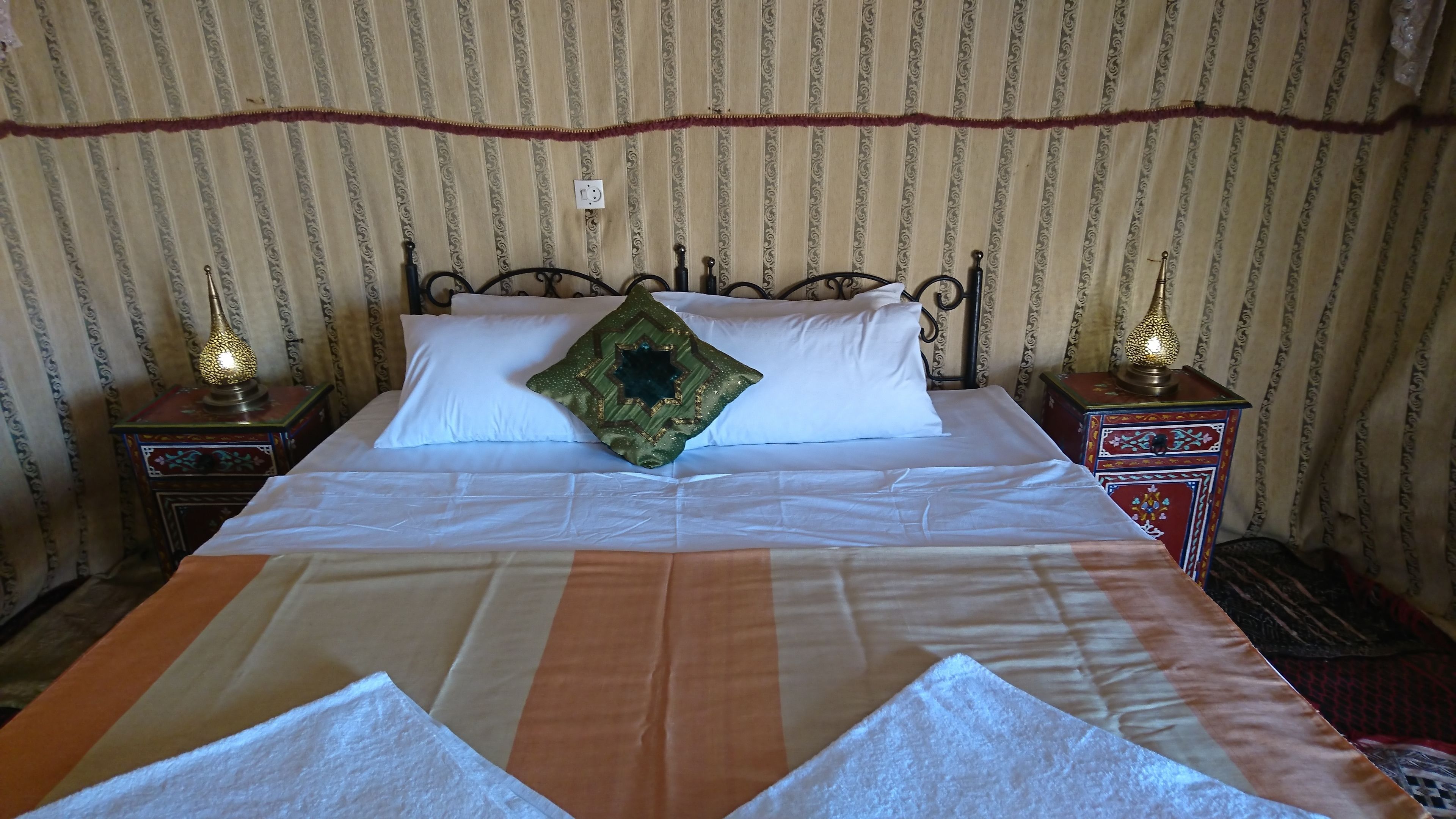 A neatly made bed with white linens and a green star-shaped pillow, flanked by two ornate nightstands with lamps.