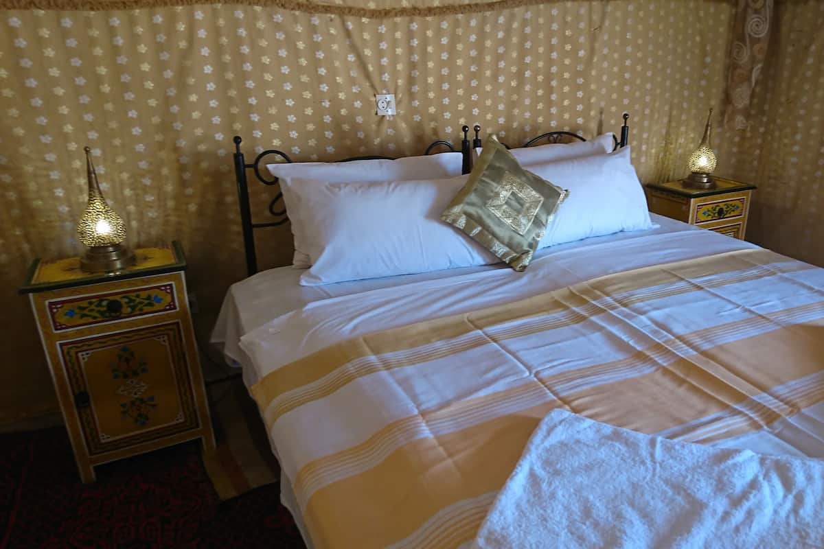 Un lit bien fait, avec une couvre-lit à rayures, deux oreillers et deux lampes de chevet sur des tables de nuit.