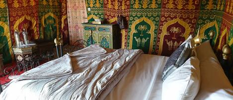 A bed with a patterned bedspread, a decorative headboard, and a wall with intricate tapestry designs.