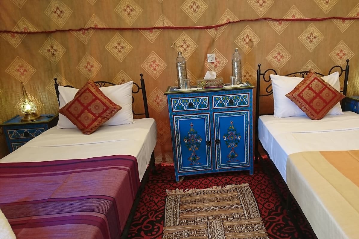 Une chambre avec deux lits, une armoire bleue ornée de motifs décoratifs et un tapis à motifs.