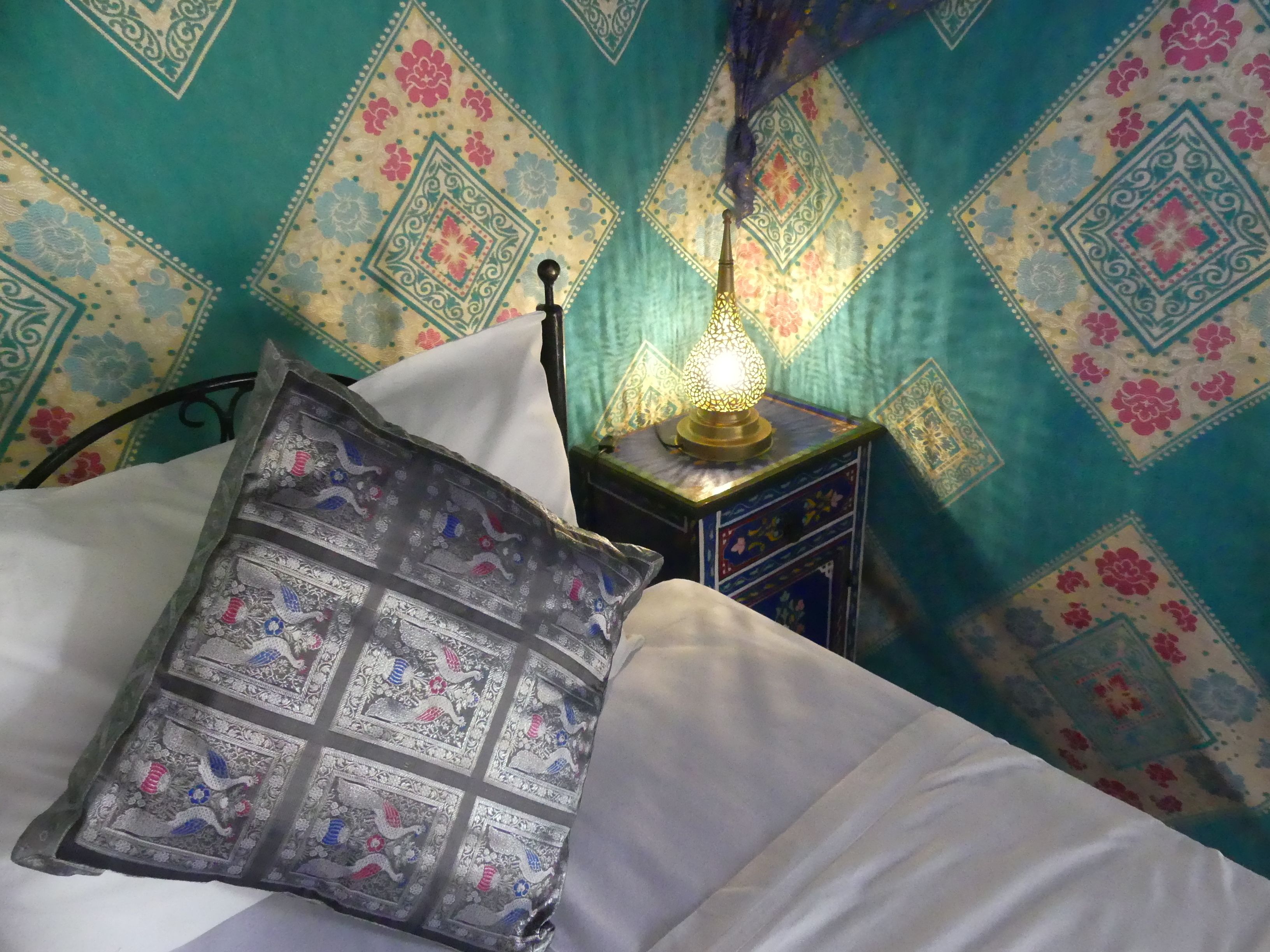 A bed with a patterned pillow and a nightstand with a decorative lamp.