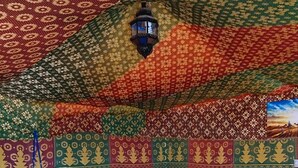 Een kamer met een gedessineerd plafond, een bed met witte beddengoed, een nachtkastje en een wandlamp.